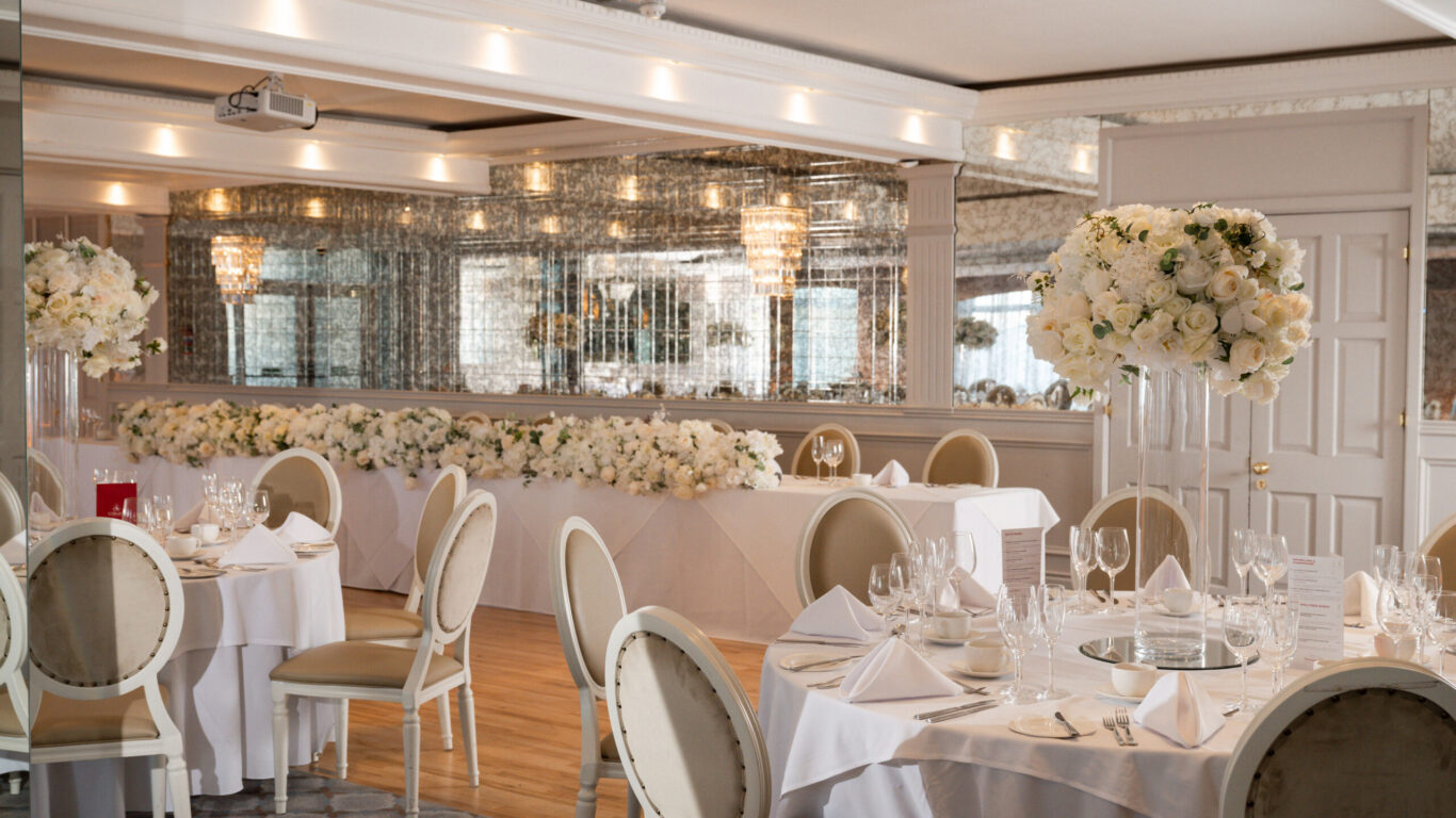 Elegant hotel dining hall with floral centrepieces, round tables, crystal chandeliers, perfect for weddings and events.