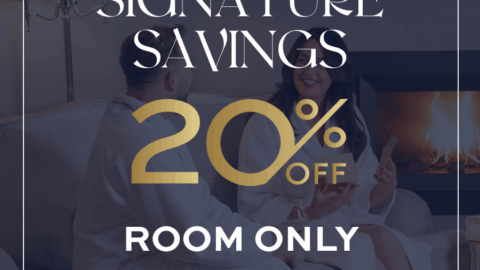 Hotel promotion ad with &ldquo;Signature Savings 20% Off Room Only&rdquo; text over an image of two people in bathrobes sitting on a couch beside a fireplace.
