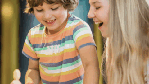 A young boy and a girl smile as they stack colorful marshmallows on a table indoors.