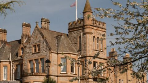 Majestic stone hotel with turret, lush gardens, and spring blossoms, offering a serene and luxurious stay in a classic setting.