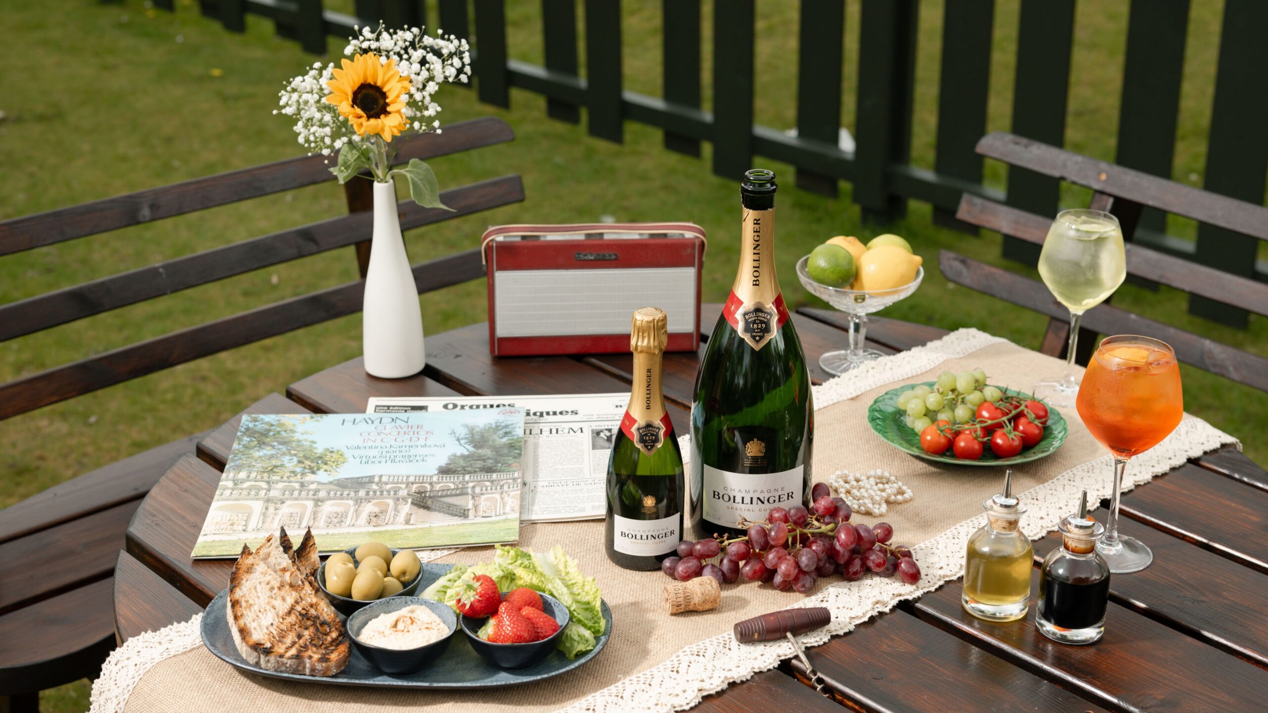 Outdoor table with champagne, fresh fruit, and rustic bread, offering a relaxing hotel garden dining experience.