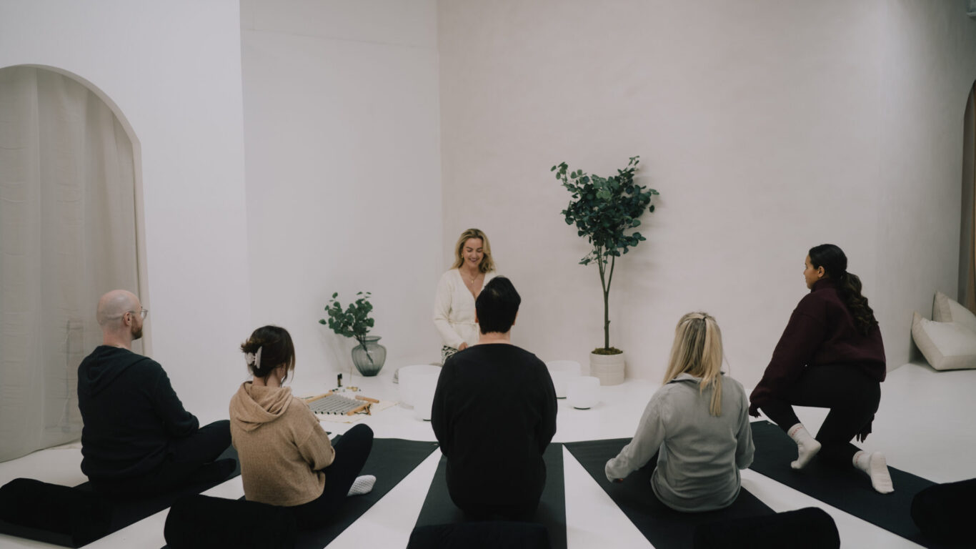 Guests enjoy a serene yoga class in a peaceful, minimalist room with white walls and greenery, enhancing relaxation.
