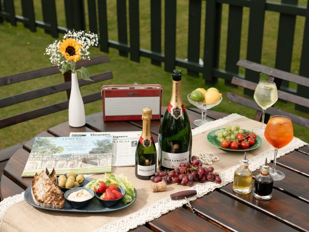 Elegant outdoor table with champagne, fresh fruit, appetisers, and flowers at luxury hotel garden setting.