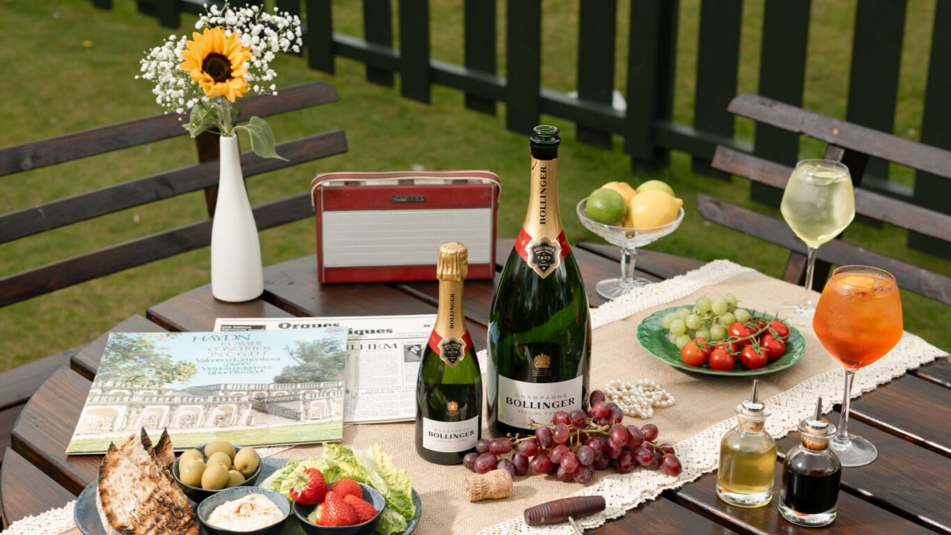 Elegant outdoor table with champagne, fresh fruit, appetisers, and flowers at luxury hotel garden setting.