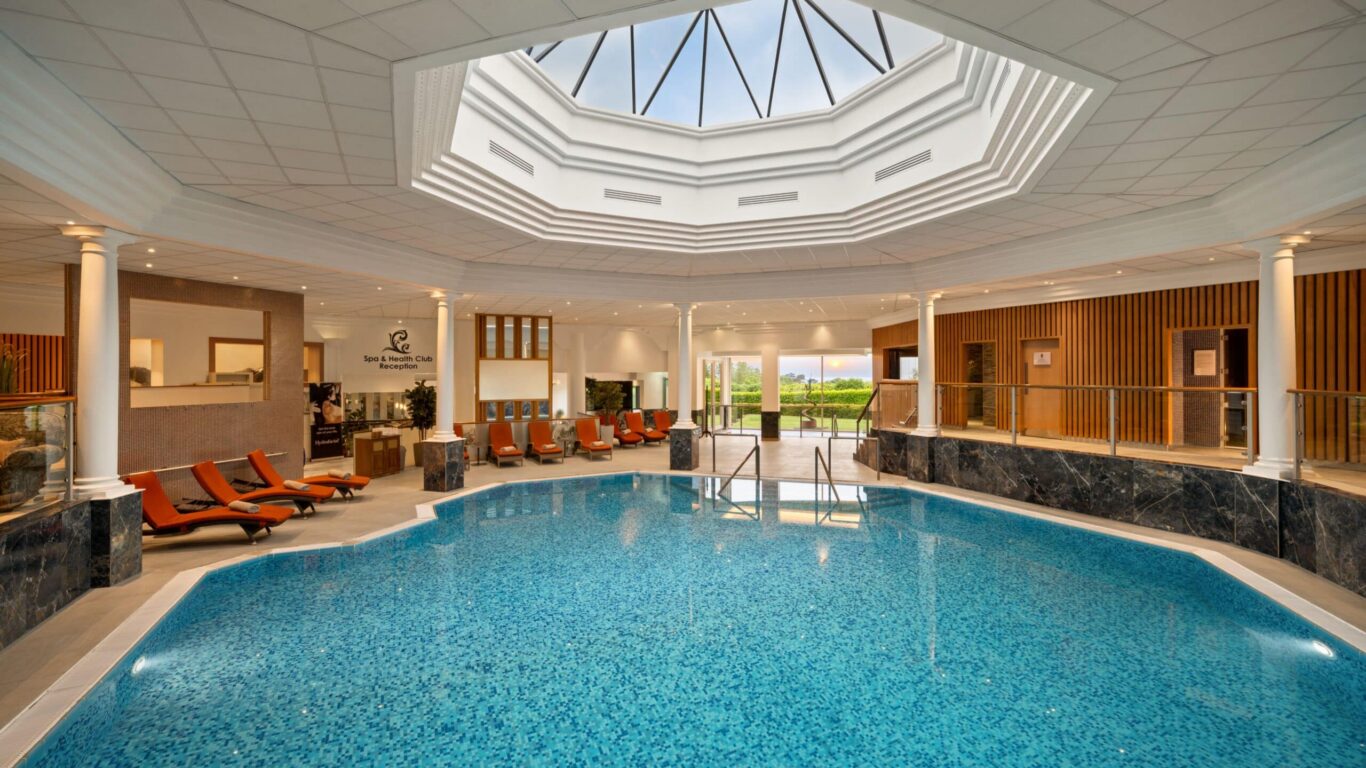 Experience luxury with the indoor pool and spa at our hotel, featuring lounge chairs and sunlit spaces for ultimate relaxation.