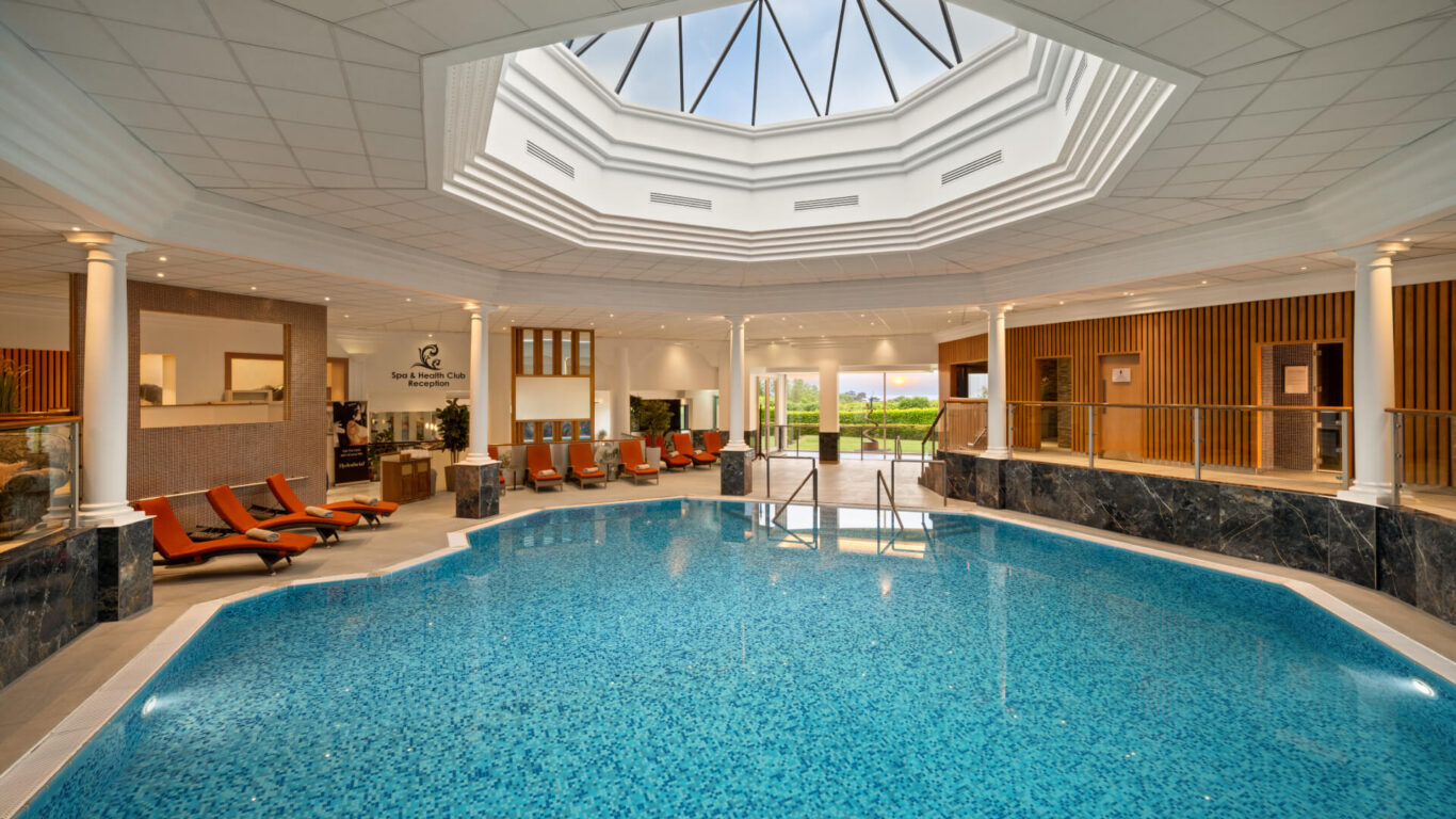 Luxurious indoor pool with skylight, sun loungers, serene ambiance at spa hotel. Relaxation and comfort await.